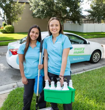merry maids holding cleaning supplies outside near a merry maids car